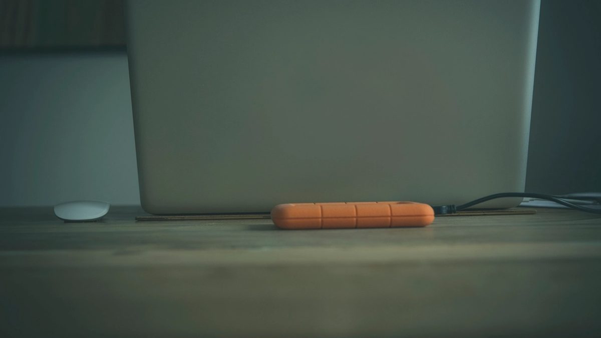 Portable external hard drive standing next to a laptop on a desk, used as a photo library backup